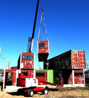 crane lifting red train container on top of other containers