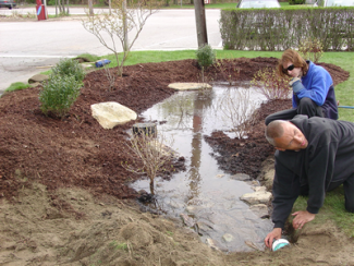 two people inspecting pooled water in mulched area