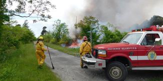 two people standing next to fire department truck watching a fire