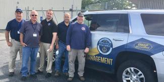 Staff standing next to a DEM suv