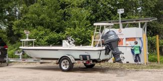 A child stands in front of a boat washing station and next to a boat on a trailer at Worden's Pond